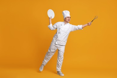 Photo of Portrait of happy confectioner in uniform holding plate and whisk on orange background