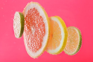 Photo of Slices of different citrus fruits in sparkling water on pink background