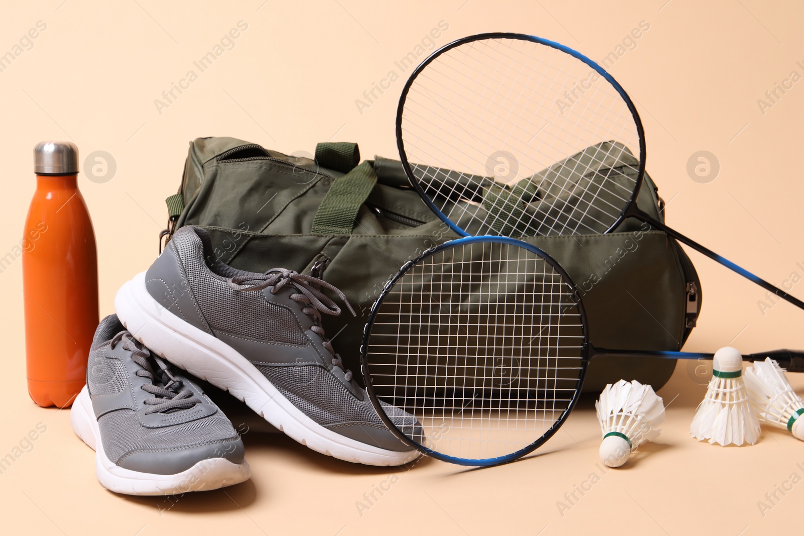 Photo of Badminton set, bag, sneakers and bottle on beige background