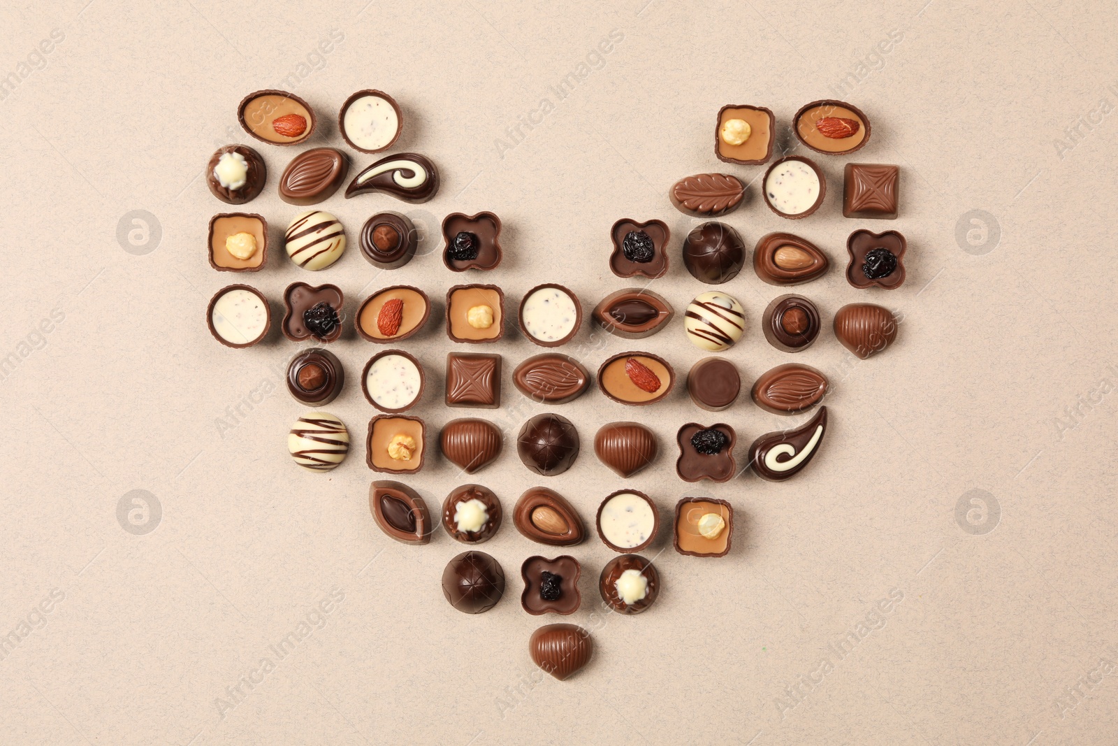 Photo of Heart made with delicious chocolate candies on beige background, top view