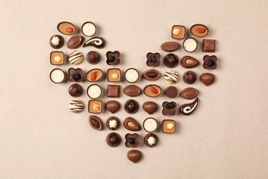 Heart made with delicious chocolate candies on beige background, top view