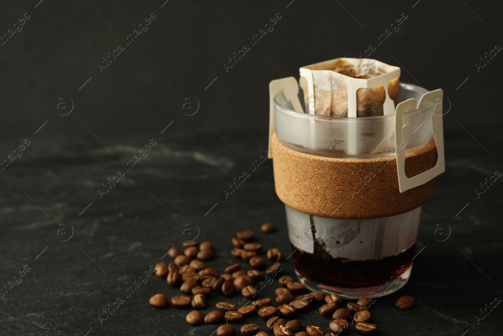 Photo of Glass cup with drip coffee bag and beans on black table, closeup