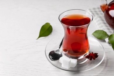 Photo of Glass of traditional Turkish tea and sugar cubes on white wooden table, closeup. Space for text