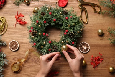 Photo of Florist making beautiful Christmas wreath at wooden table, top view