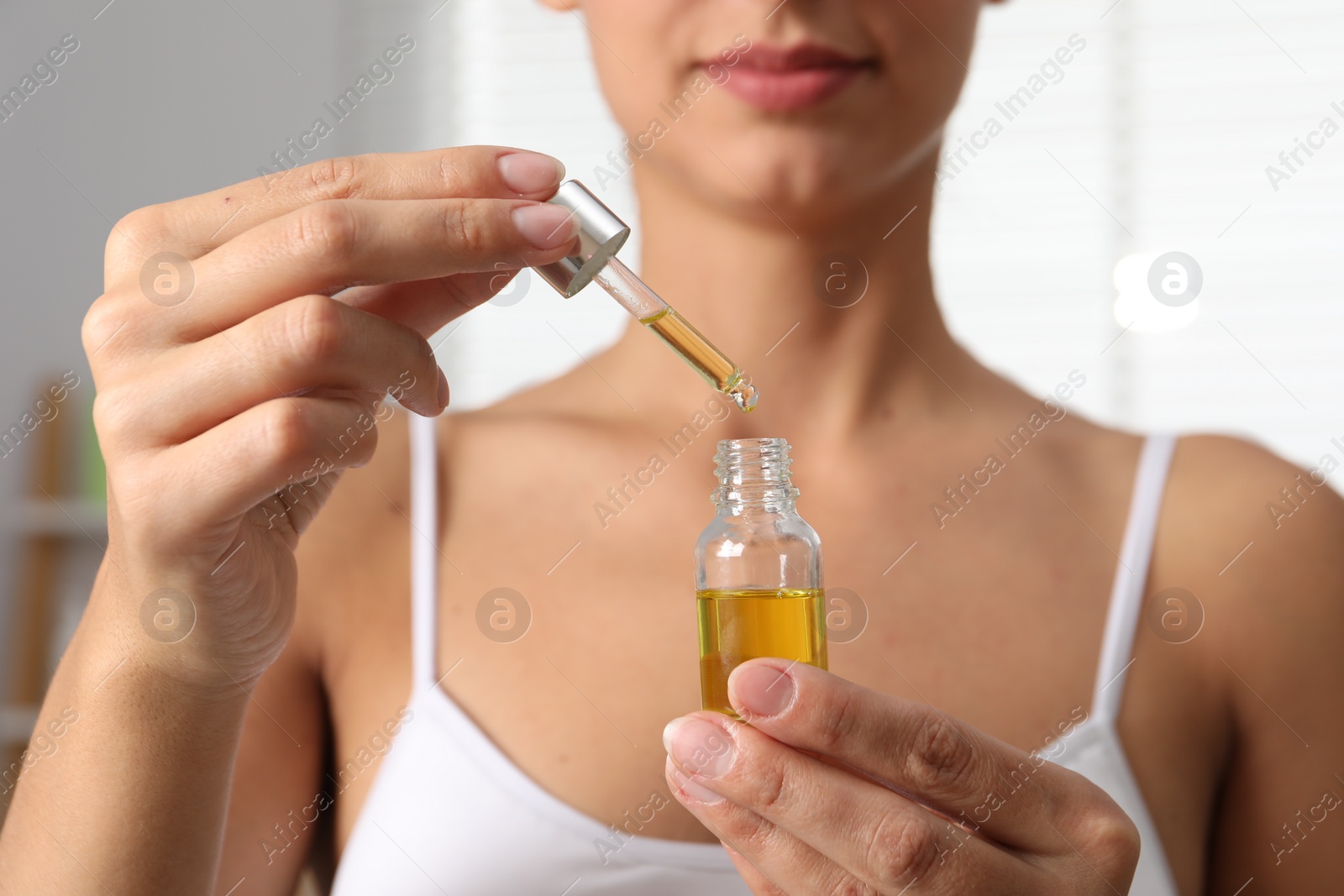 Photo of Woman with bottle of cosmetic serum on blurred background, closeup