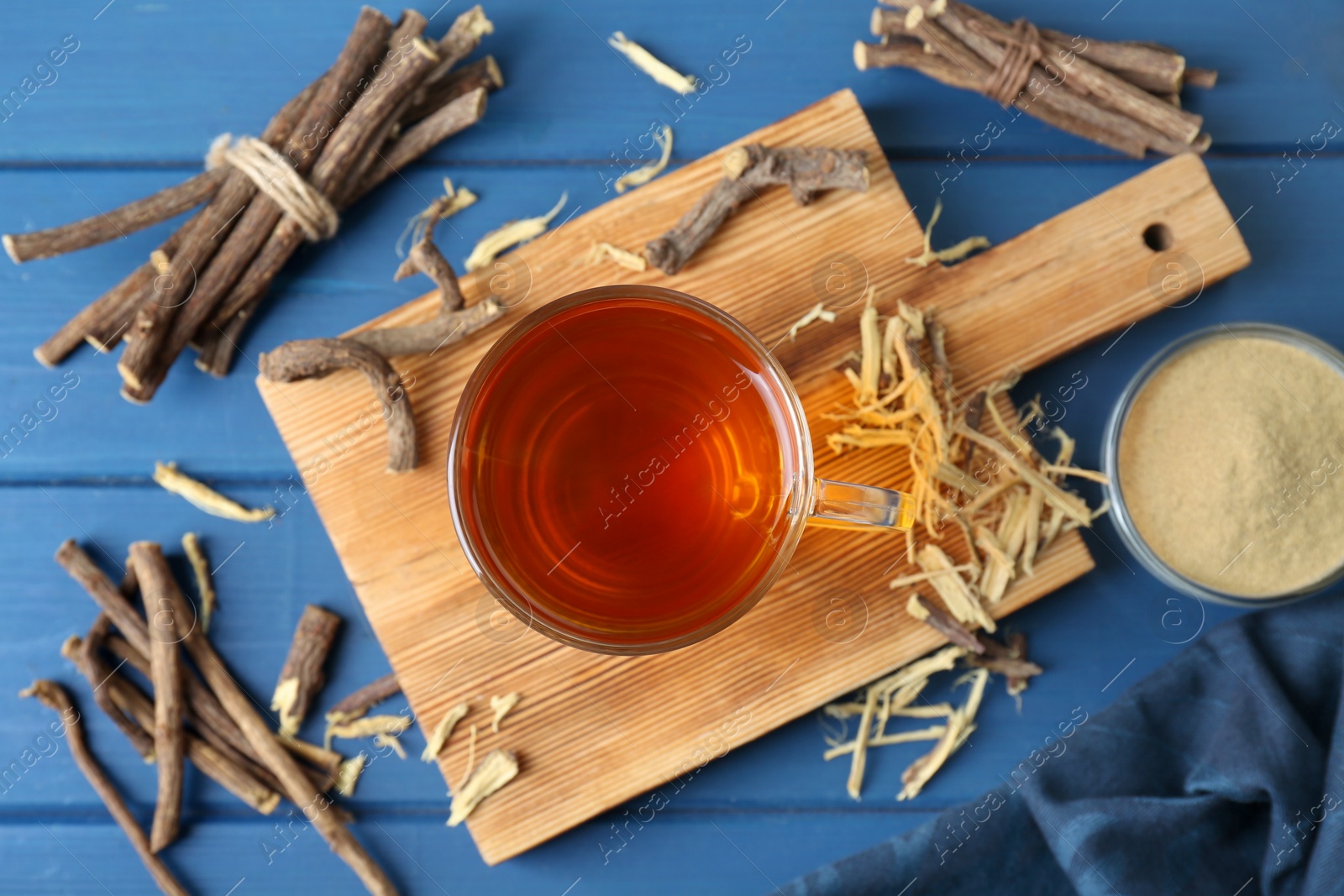 Photo of Aromatic licorice tea in cup, dried sticks of licorice root and powder on blue wooden table, flat lay