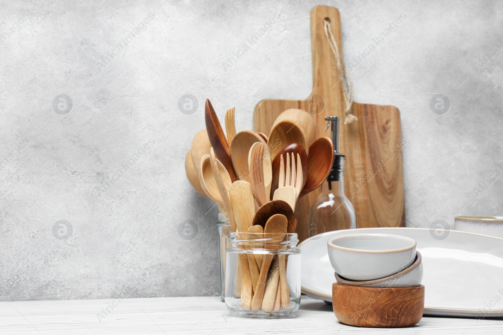 Photo of Different kitchenware and dishware on white wooden table against textured wall. Space for text