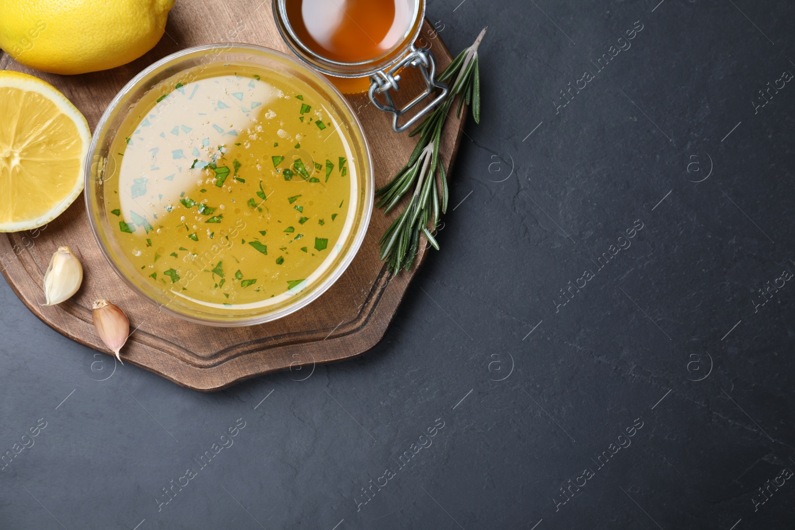 Photo of Bowl of lemon sauce and ingredients on dark table, top view with space for text. Delicious salad dressing