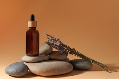 Photo of Bottle of face serum, spa stones and lavender flowers on beige background, space for text