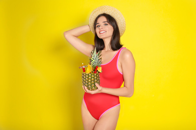 Beautiful woman in red swimsuit holding tropical cocktail on yellow background