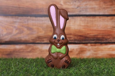Photo of Easter celebration. Funny chocolate bunny on grass against wooden background
