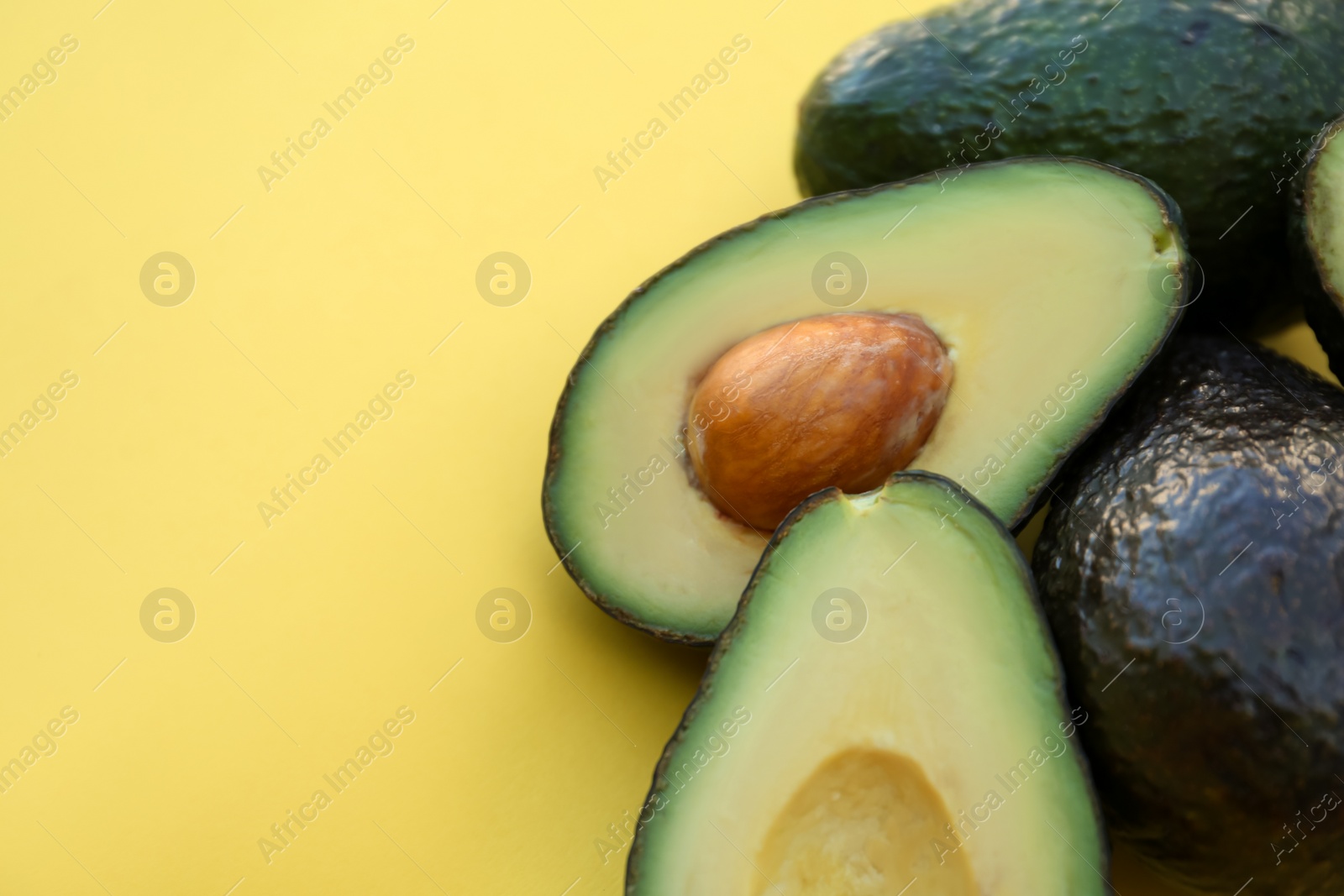 Photo of Fresh whole and cut avocados on yellow background, closeup. Space for text