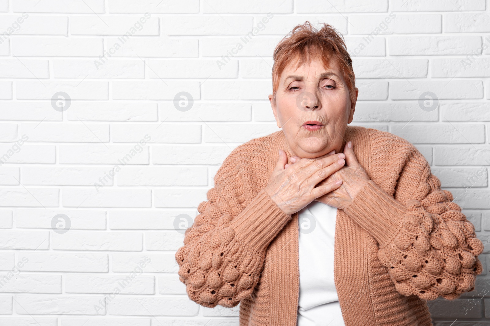 Photo of Elderly woman coughing near brick wall. Space for text