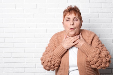 Elderly woman coughing near brick wall. Space for text