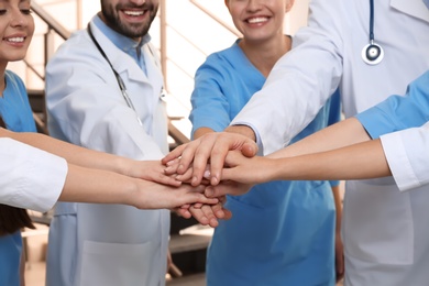 Photo of Team of medical doctors putting hands together indoors, closeup. Unity concept