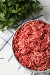 Photo of Raw ground meat in bowl and parsley on table, top view