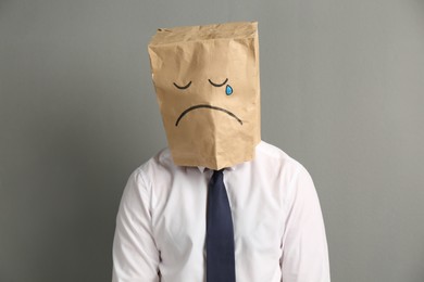 Photo of Man wearing paper bag with drawn sad face on grey background