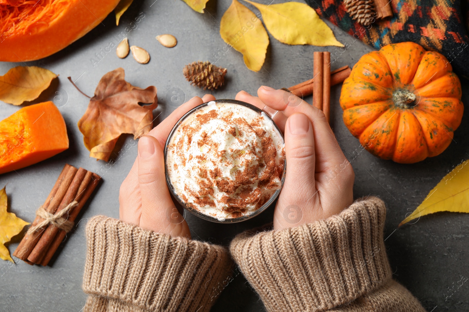 Photo of Woman holding tasty pumpkin latte at grey table, top view