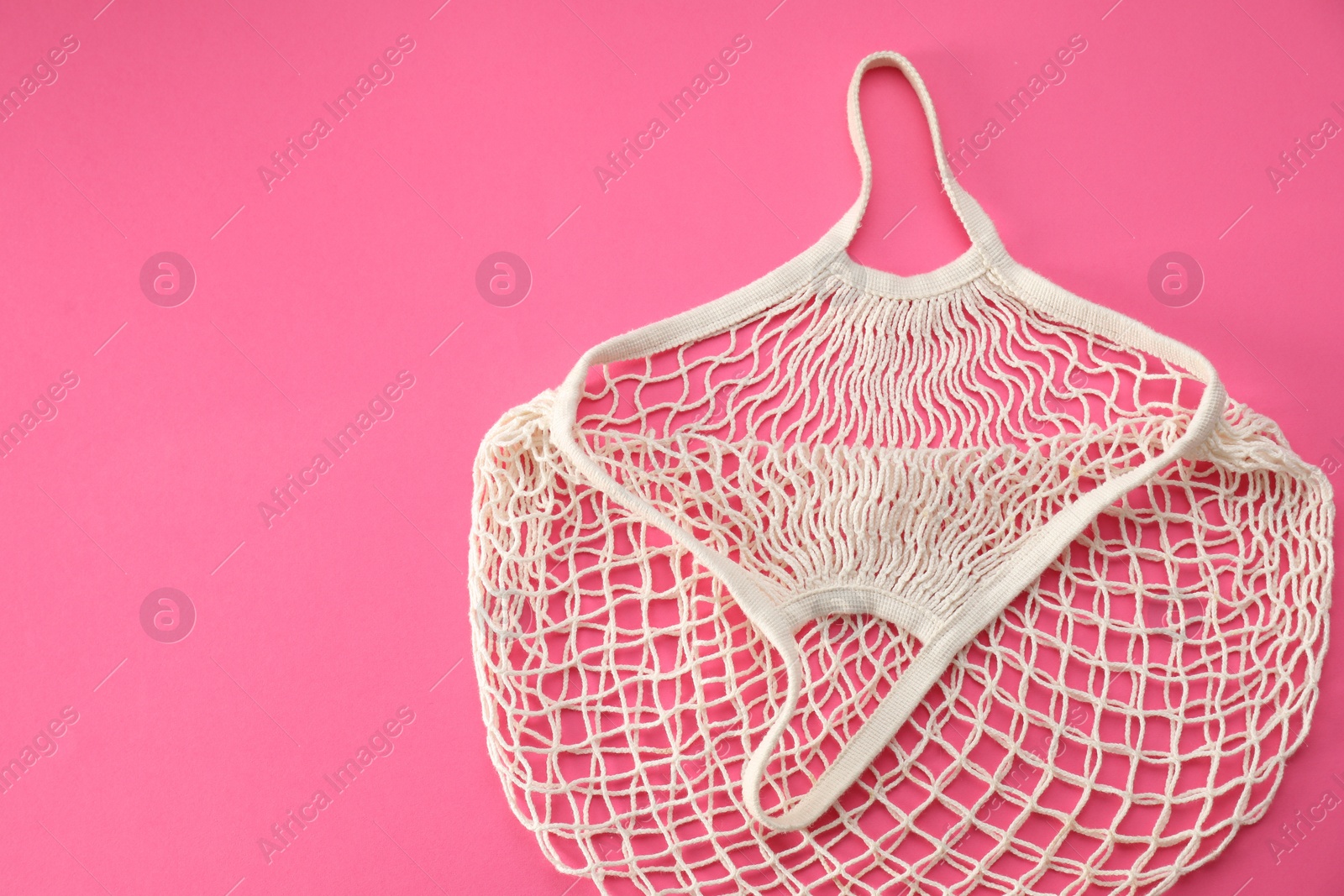 Photo of White string bag on bright pink background, top view. Space for text