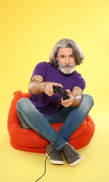 Photo of Emotional mature man playing video games with controller on color background