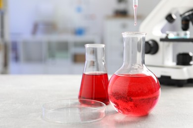 Photo of Laboratory analysis. Dripping red liquid into flask at light grey table, closeup. Space for text