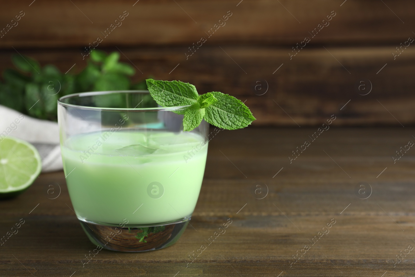 Photo of Delicious mint liqueur with green leaves on wooden table. Space for text