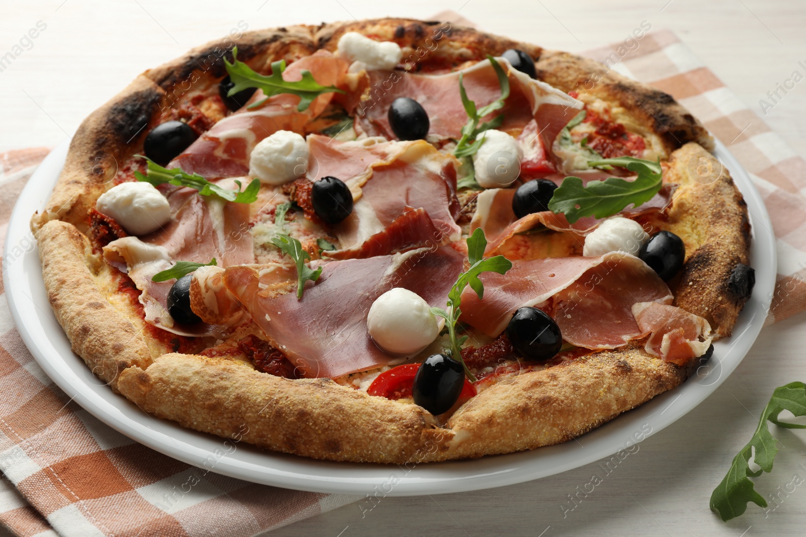 Photo of Tasty pizza with cured ham, olives, mozzarella cheese, sun-dried tomato and arugula on table, closeup