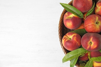 Photo of Wicker bowl with tasty peaches on white wooden table, top view. Space for text