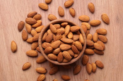 Photo of Tasty almonds in bowl on wooden table, flat lay