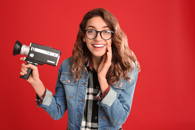 Beautiful young woman with vintage video camera on red background