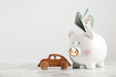 Photo of Piggy bank with dollar banknotes and toy car on table against white background. Space for text