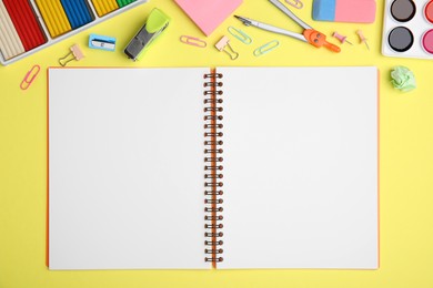 Photo of Flat lay composition with notebook and different school stationery on pale yellow background. Back to school