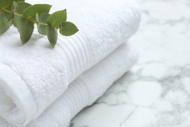 Photo of Folded terry towels and eucalyptus branch on white marble table, closeup