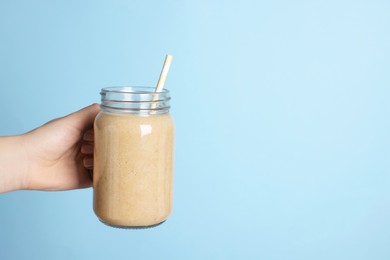 Woman holding mason jar with tasty smoothie and straw on light blue background, closeup. Space for text