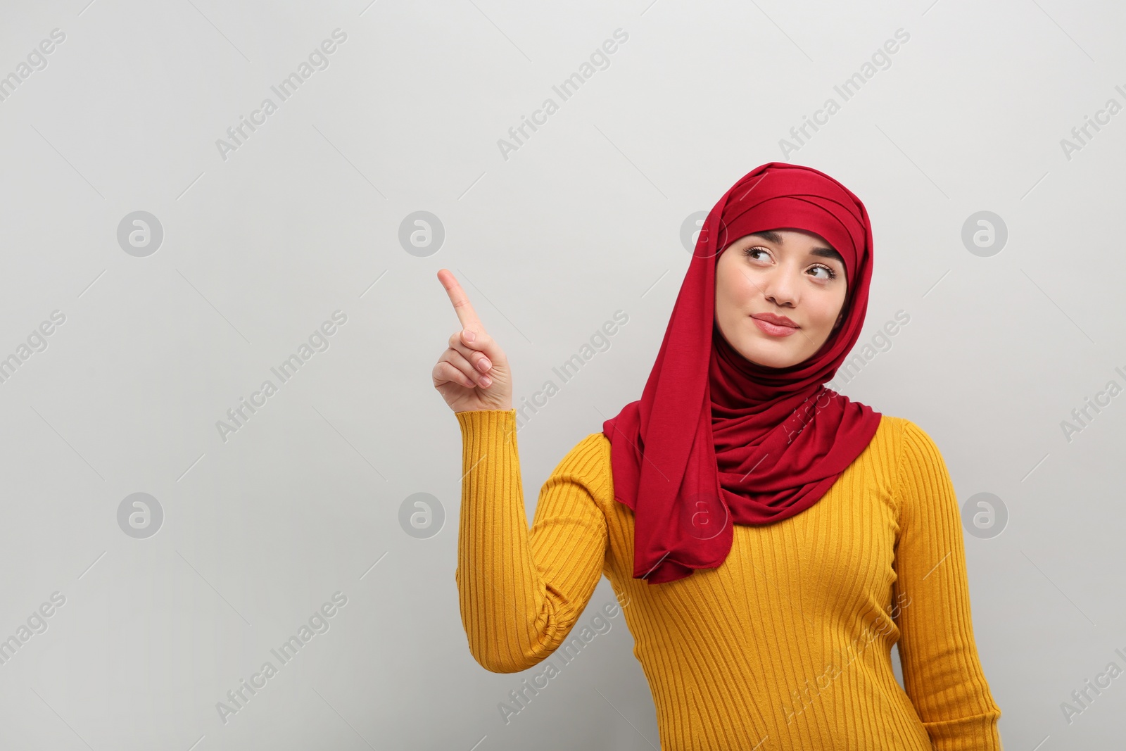 Photo of Muslim woman in hijab pointing at something on light gray background, space for text