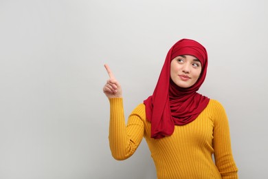 Photo of Muslim woman in hijab pointing at something on light gray background, space for text