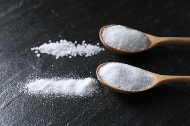 Photo of Organic salt in spoons on black table, closeup