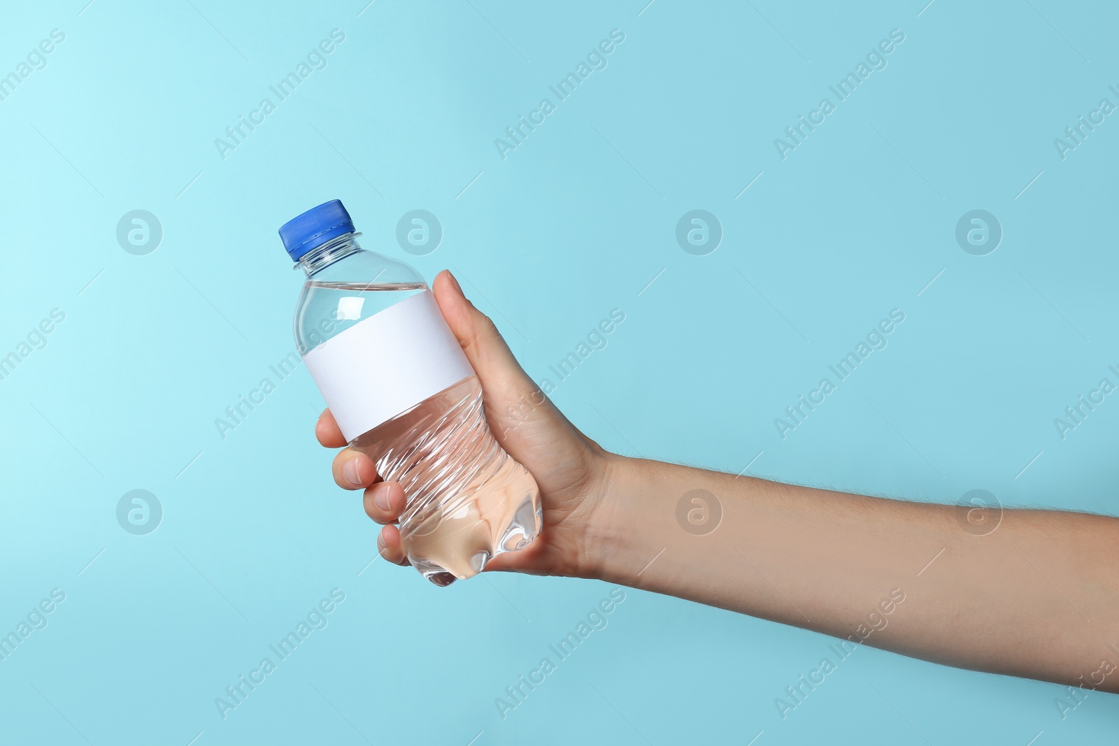 Photo of Woman holding plastic bottle of pure water with blank tag on color background