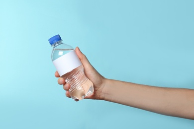 Photo of Woman holding plastic bottle of pure water with blank tag on color background