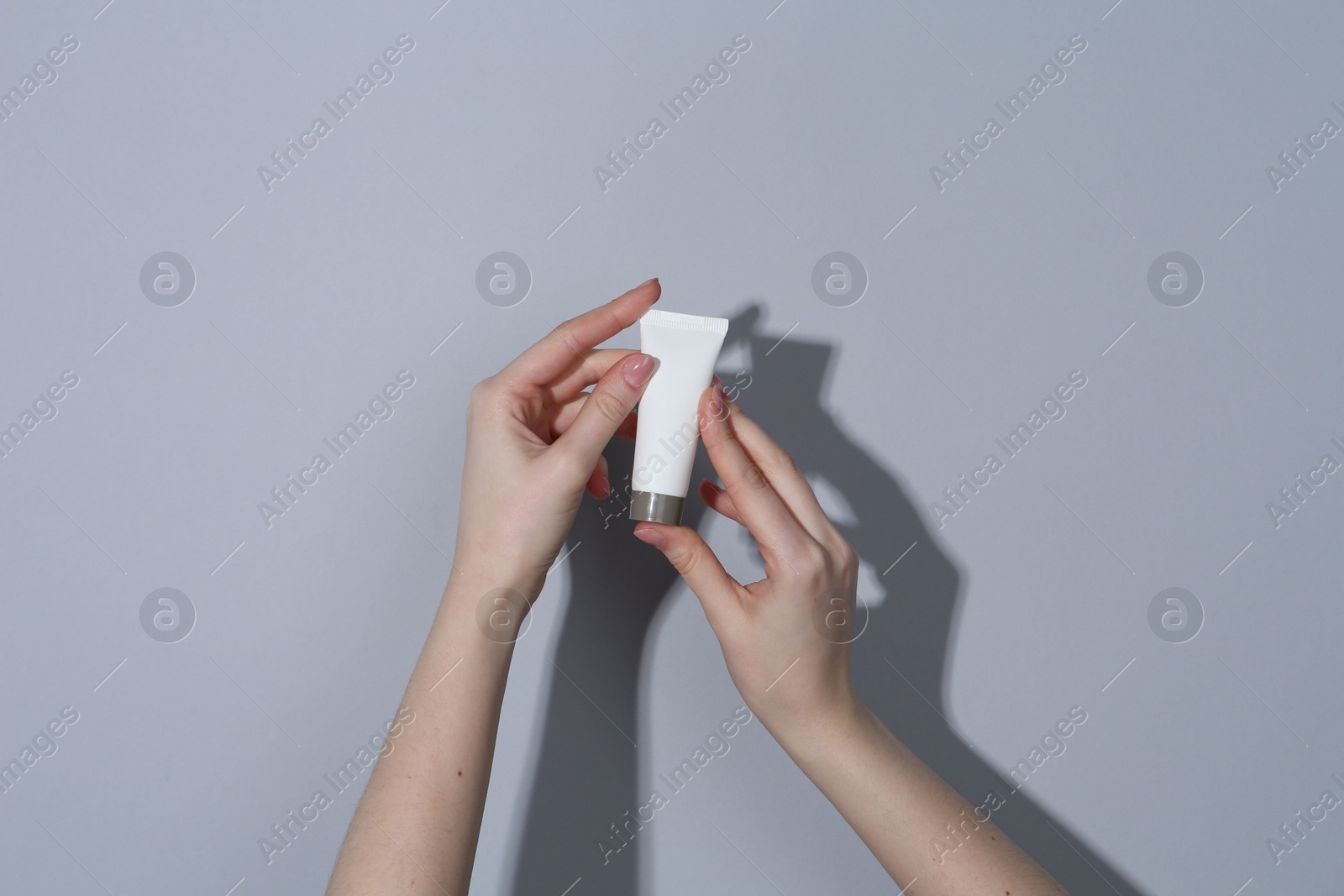 Photo of Woman holding tube of cream on grey background, closeup