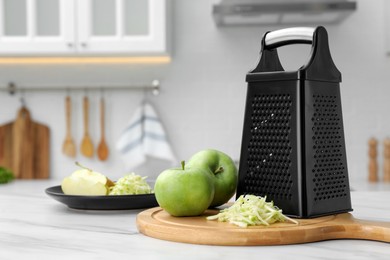 Photo of Grater and fresh ripe apples on white table in kitchen. Space for text