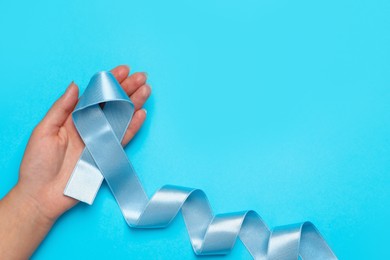 Woman holding light blue awareness ribbon on color background, top view. Space for text