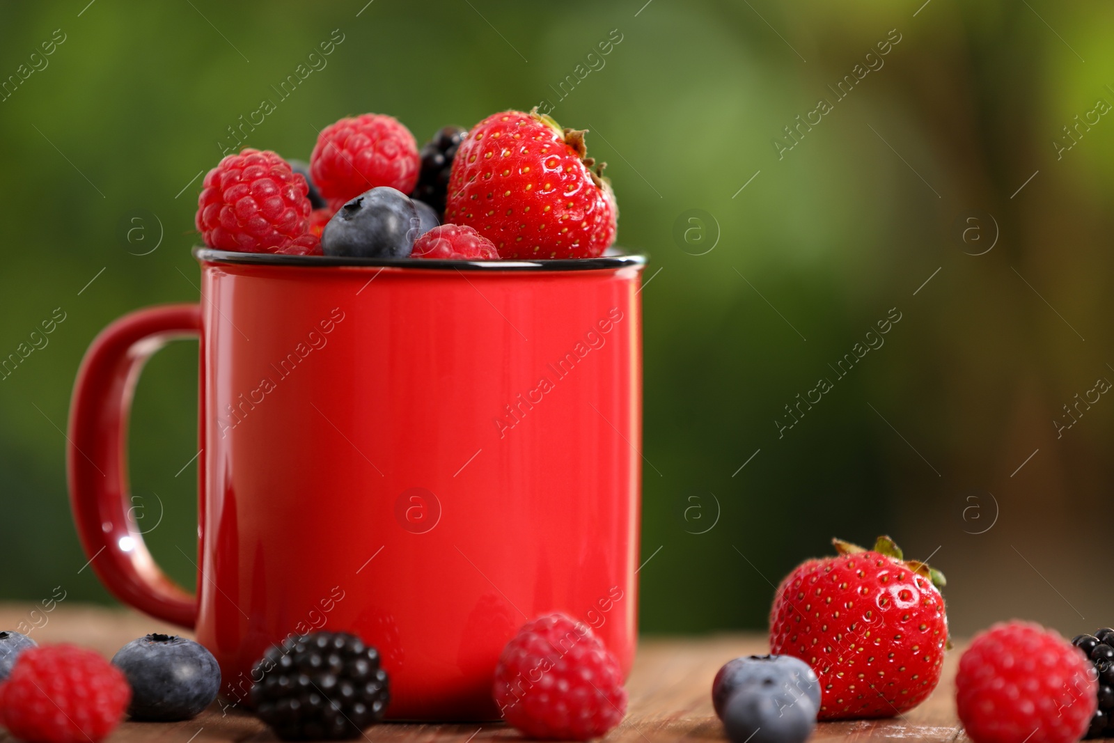 Photo of Mug with different fresh ripe berries on table outdoors