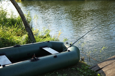 Photo of Inflatable boat with rod for fishing near wooden pier at riverside