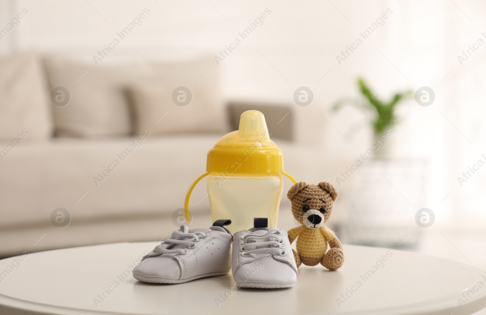 Photo of Baby bottle and shoes near toy bear on white table in room. Maternity leave concept