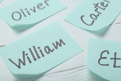 Photo of Paper stickers with different names on white wooden table, closeup. Choosing baby's name