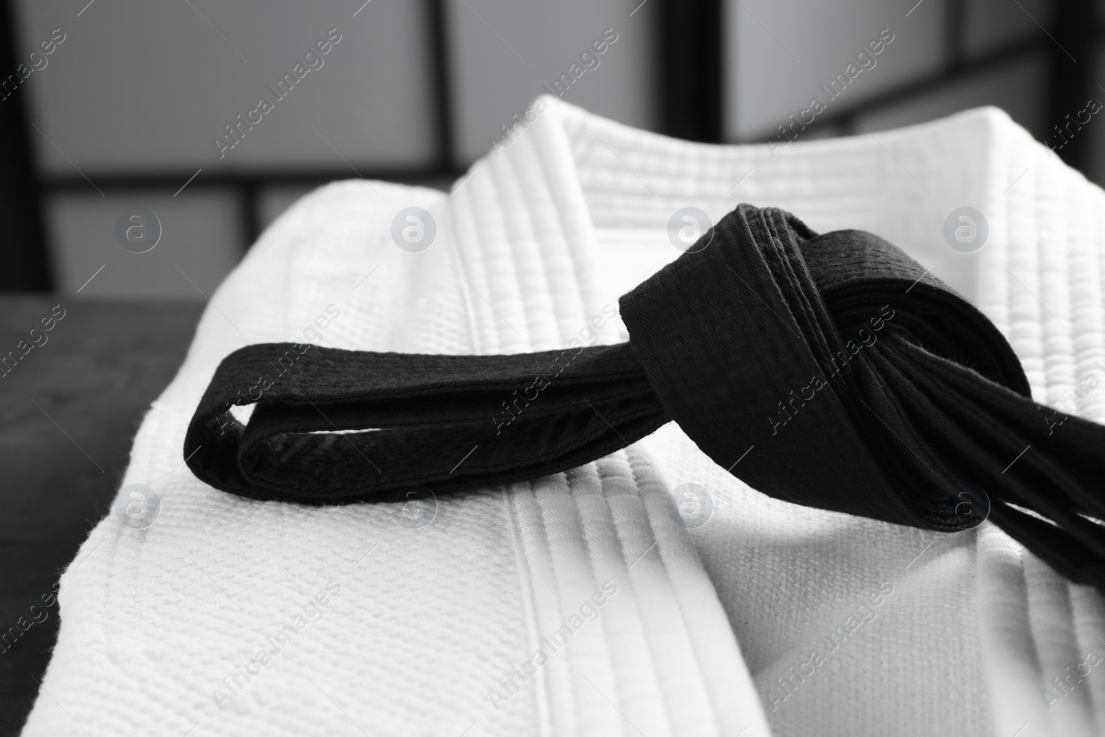 Photo of Martial arts uniform with black belt on table indoors, closeup
