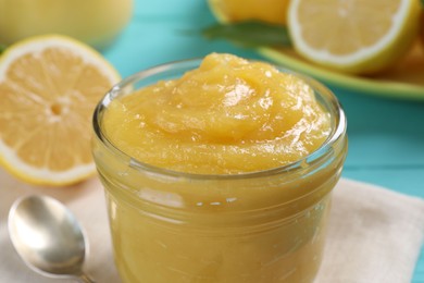 Delicious lemon curd in glass jar, fresh citrus fruit and spoon on table, closeup