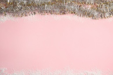Shiny tinsel and snow on pink background, top view. Space for text