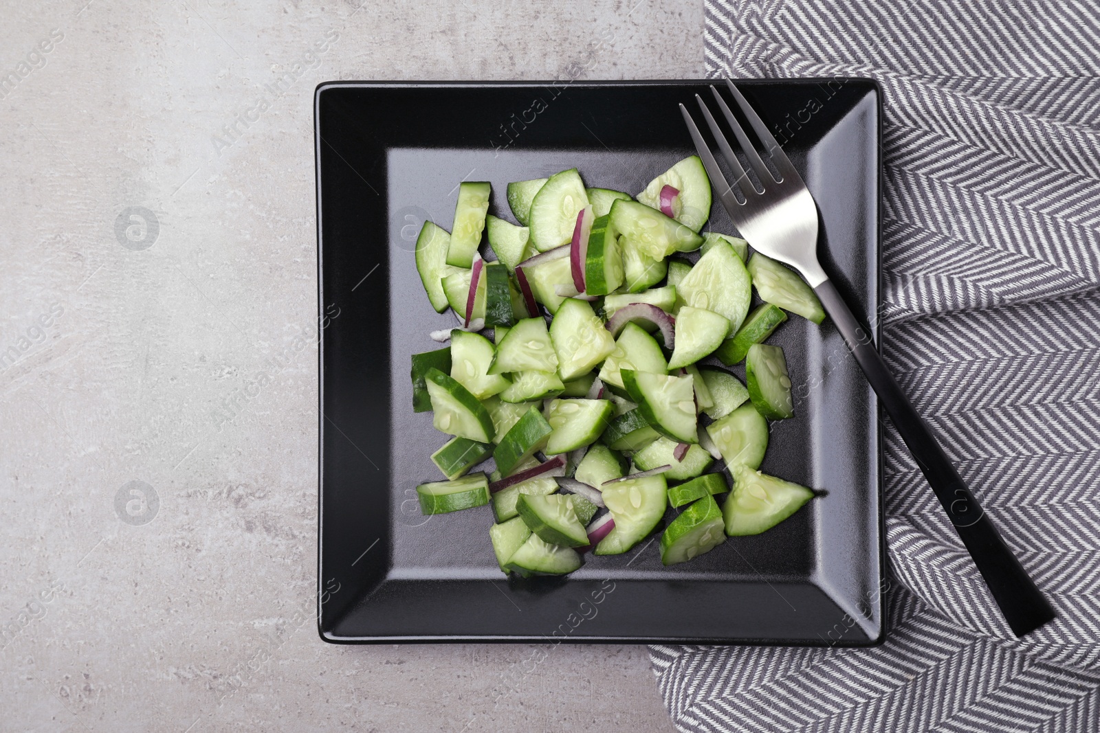 Photo of Plate of vegetarian salad with cucumber and onion served on table, flat lay